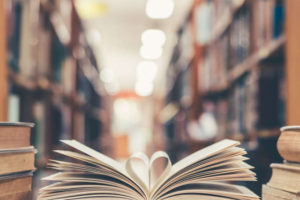 Open book on desk with center pages curled into a heart and background of bookshelves.