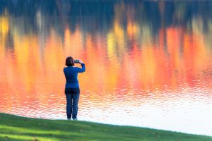 Woman photographing lake with autumn reflections.