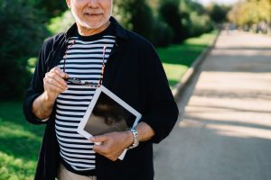 Man with sunglasses and tablet walking a park path.