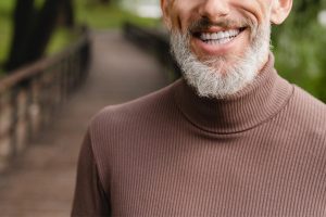 Senior man with beard smiling in a park.
