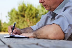 Man writing at a park picnic table.