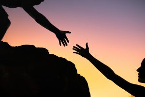 Silhouette of woman reaching for help stepping up on a mountain hike.