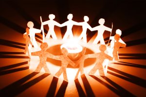 A chain of paper dolls hand in hand in a circle, glowing before a central source of light