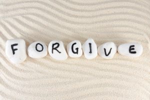 Painted rocks that spell “Forgive” resting in patterned sand.